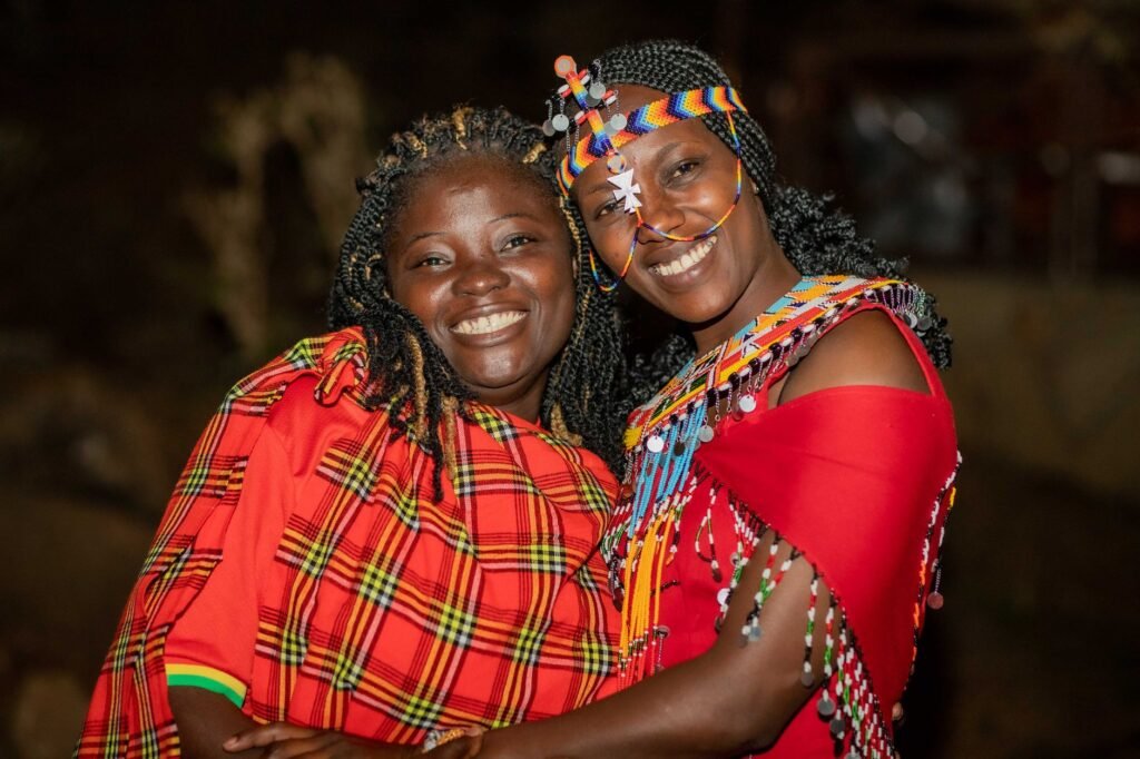 Two smiling African women in vibrant traditional Maasai clothing celebrating together.