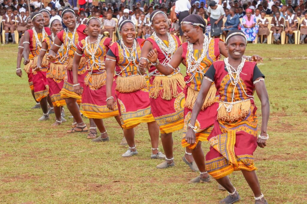A group of women performing a traditional tribal dance outdoors with smiles and colorful costumes.