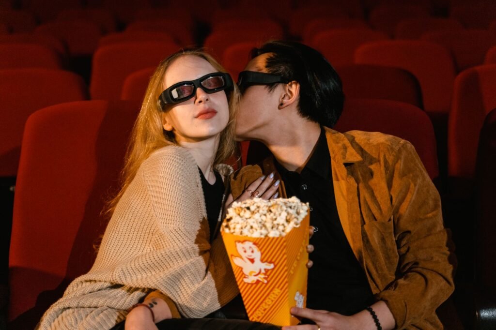 Young couple enjoying a movie date with popcorn in a theater, wearing 3D glasses.