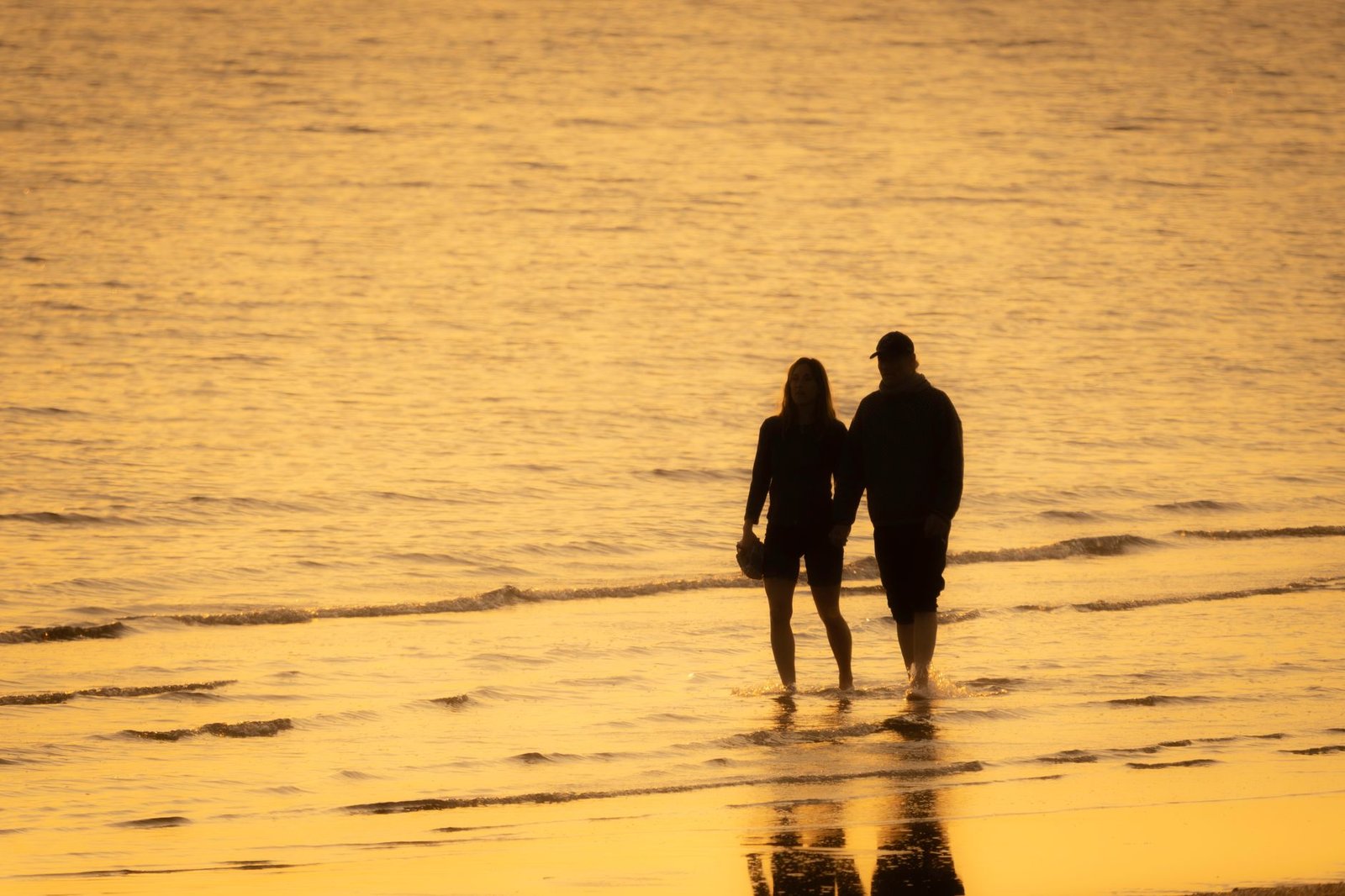 A couple holding hands while walking on the beach at sunset, creating a romantic silhouette.