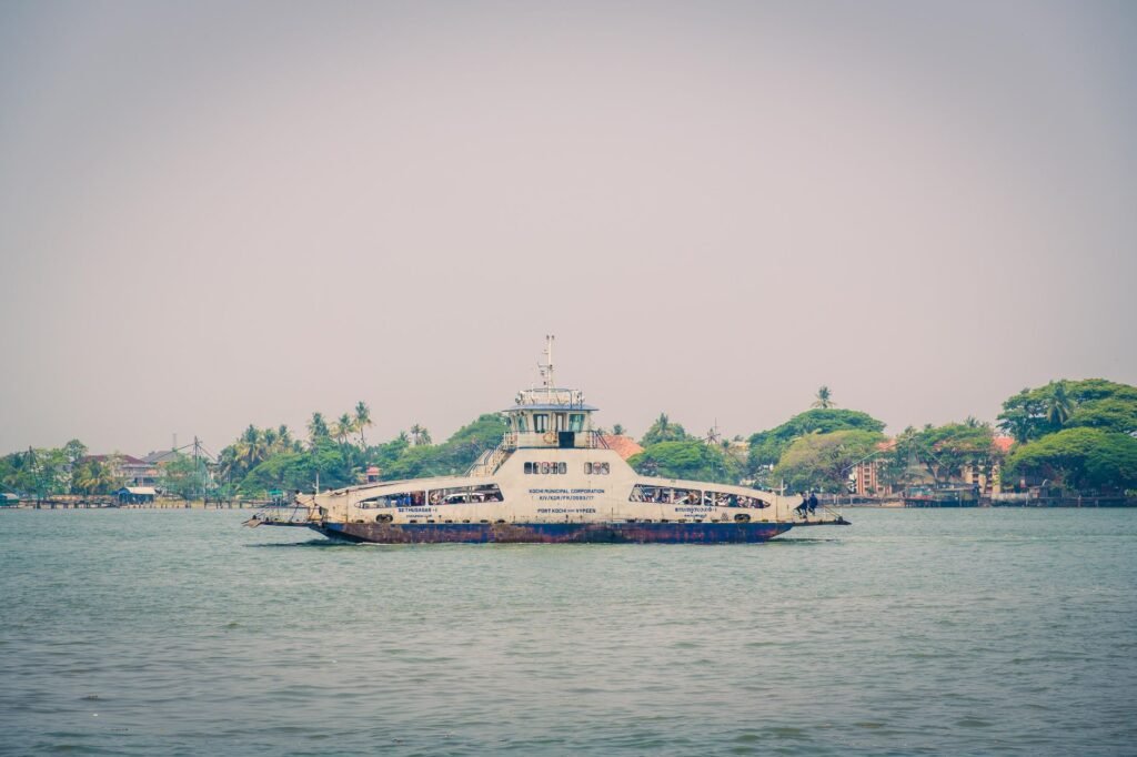 A vintage ferry navigates along a tropical coastline near Kochi, showcasing serene coastal vibes.