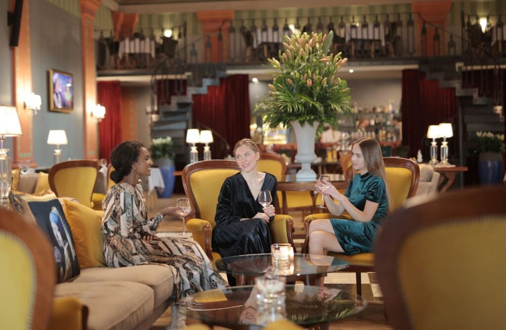 Three women socializing in a stylish hotel lounge with drinks in hand.