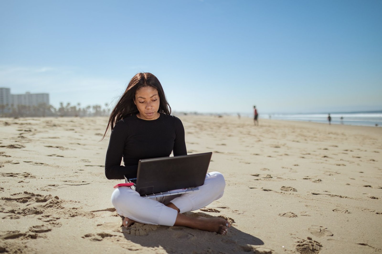 Young woman working remotely on a beach with her laptop, embracing the digital nomad lifestyle.