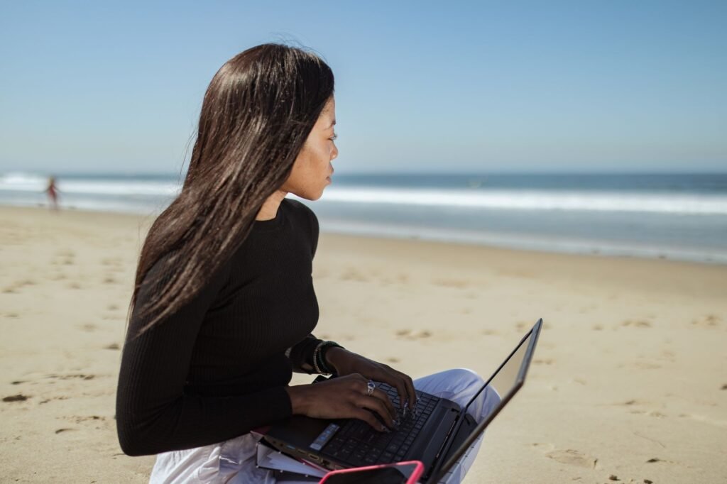 Woman working with a laptop on a sandy beach, enjoying a sunny day at the seaside.