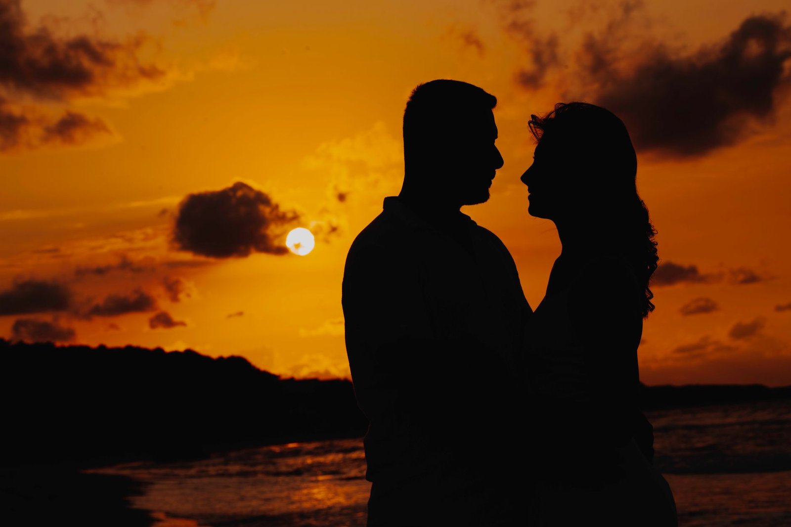 Silhouette of a couple embracing on a beach at sunset, with warm, dramatic colors and a scenic sky.