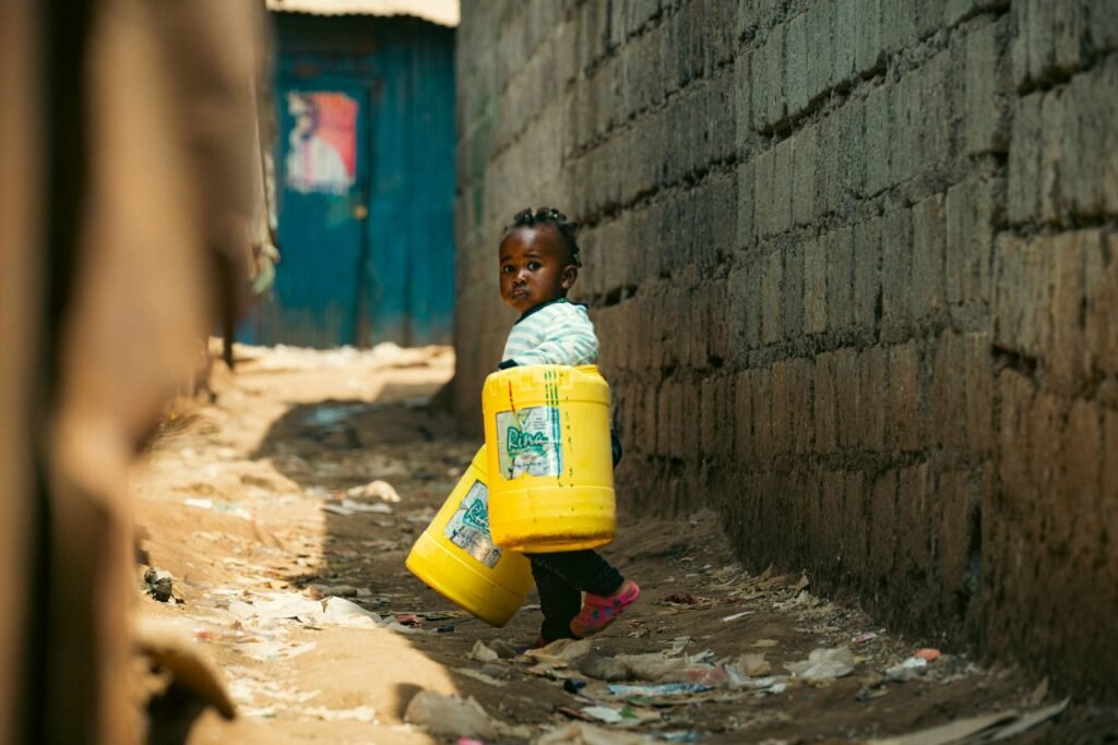 A young child carrying yellow containers through a narrow alley in Nairobi, Kenya.