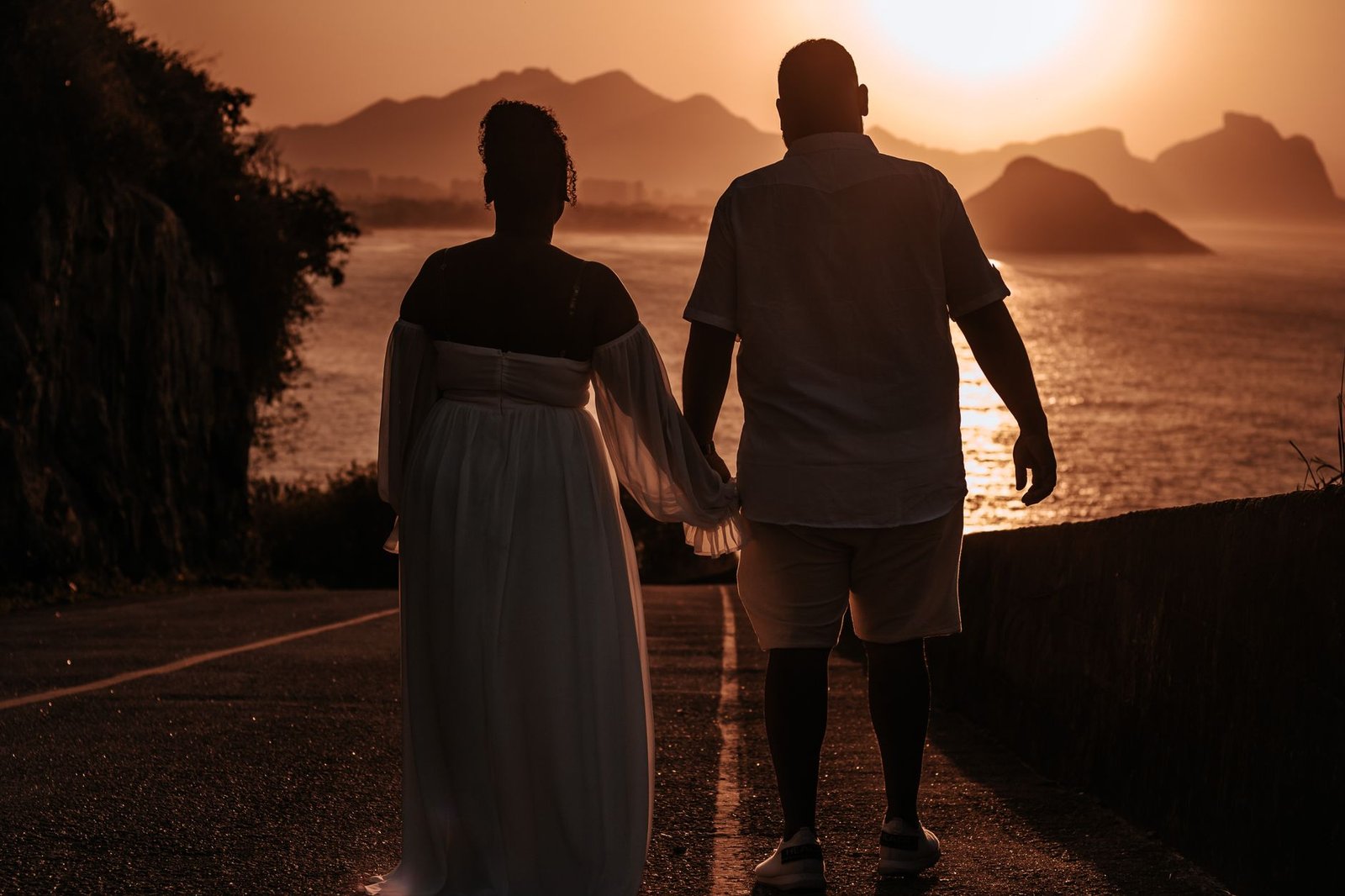 A couple walking hand in hand at sunset on a scenic coastal path, silhouetted against the sea.