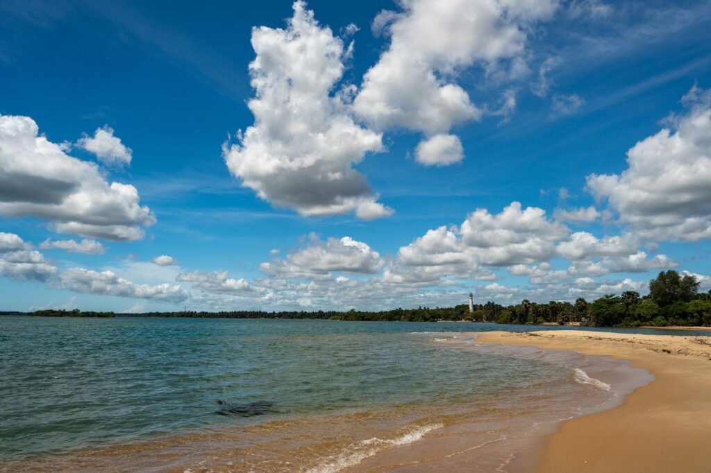 A serene beach view at Batticaloa Lagoon, Sri Lanka with bright clouds under a vivid blue sky.