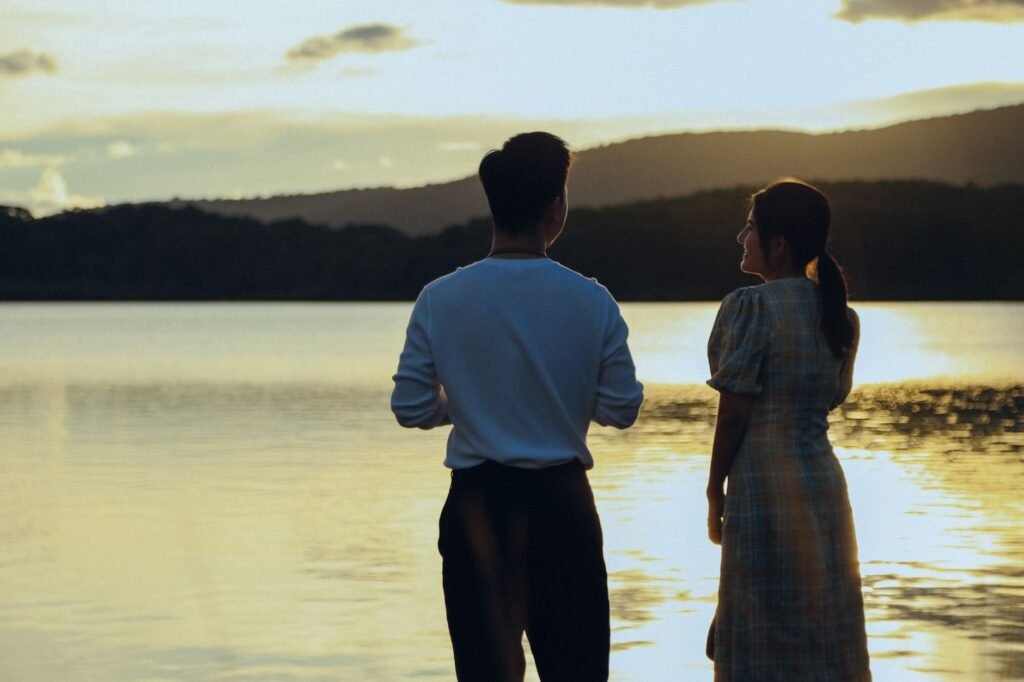 A couple enjoys a serene sunset by the lake, creating a romantic ambiance.