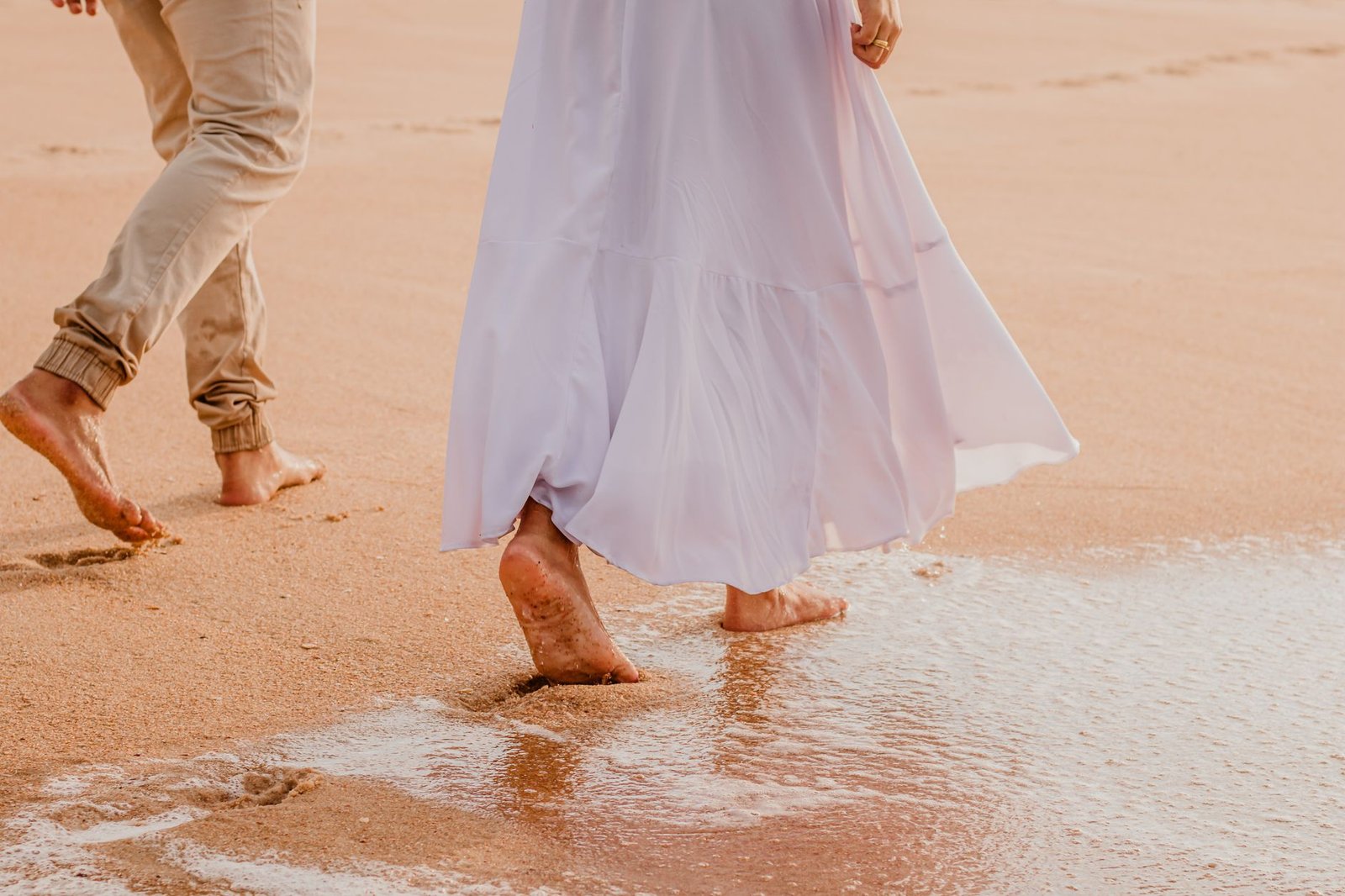 Couple walking barefoot on a sandy beach, enjoying a calm day at the seaside.