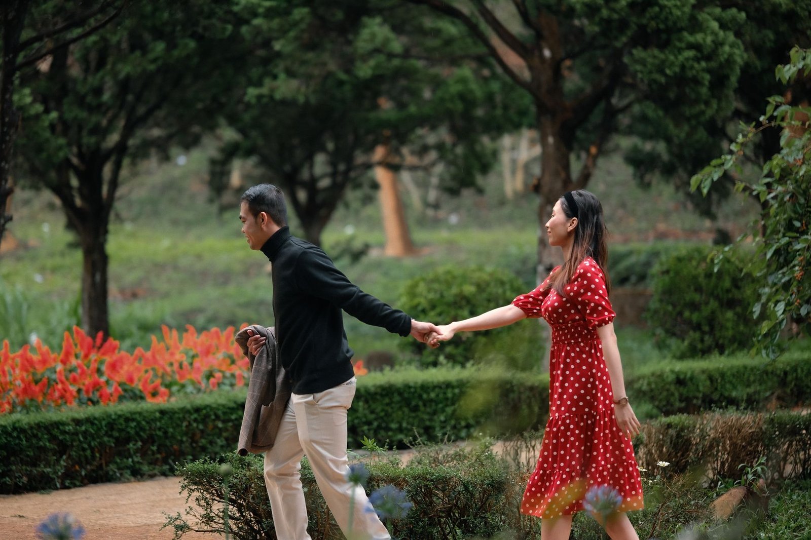Couple holding hands walking through a picturesque garden, showcasing love and serenity.