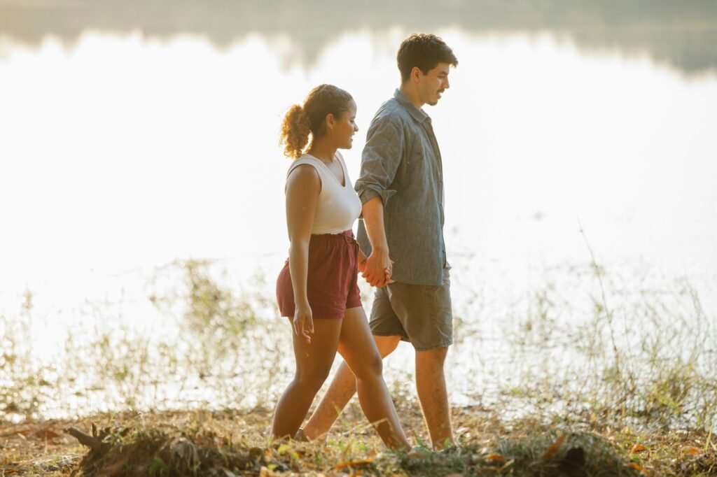 Side view of beloved young multiracial couple walking and holding hands during romantic date near lake at sunset