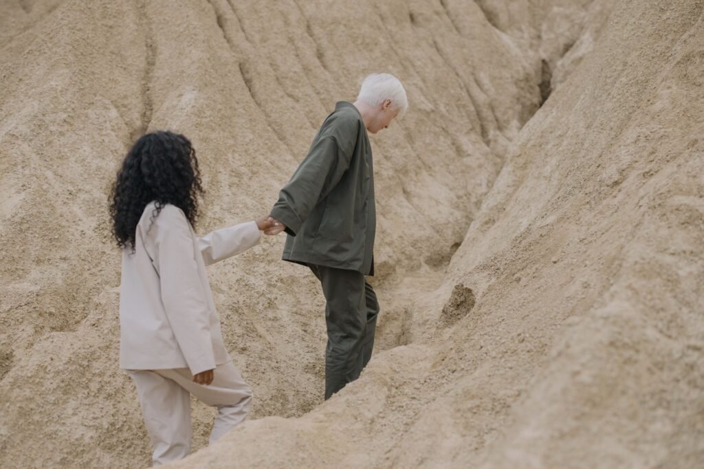 A diverse couple holding hands while walking through a sandy, desert-like terrain. Represents togetherness and adventure.