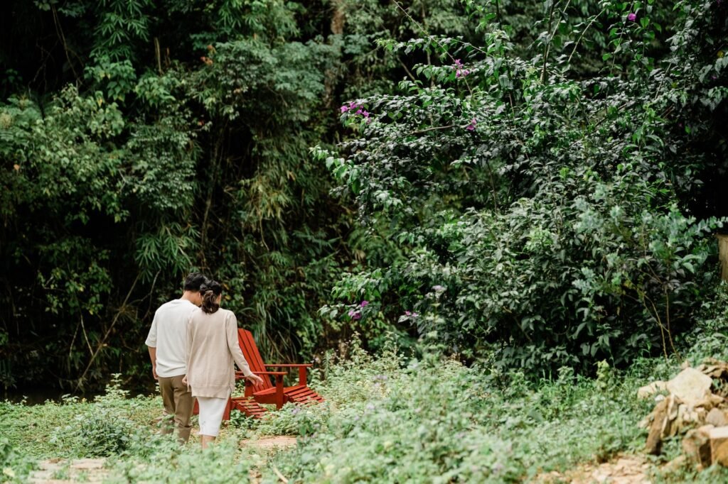 A serene scene of a couple walking in a lush, green rural setting with red chairs.
