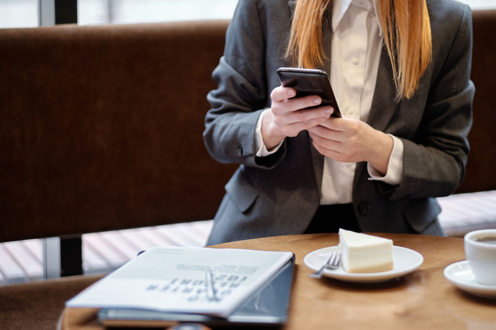 Businesswoman using smartphone in a café, with slice of cake and coffee.