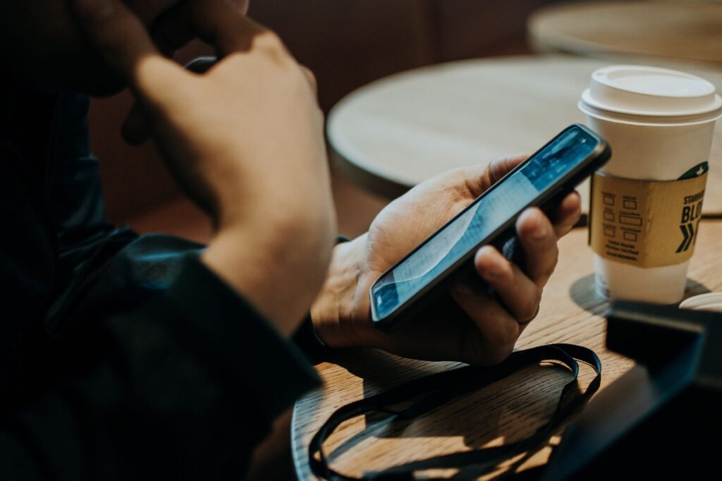 Close-up of a person using a smartphone in a cozy coffee shop, enjoying a beverage.