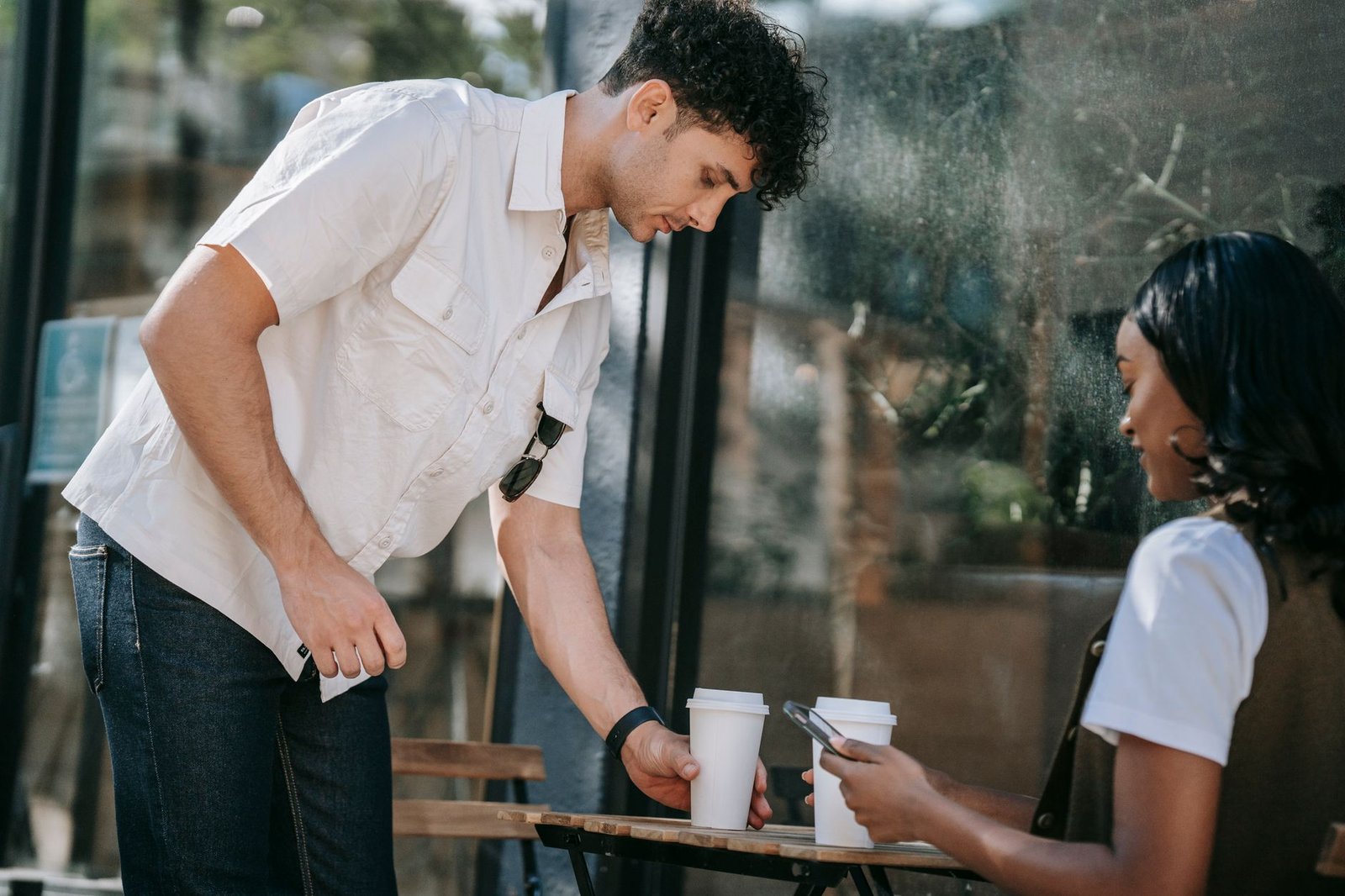 A young interracial couple enjoys coffee at an outdoor cafe. Daytime setting.