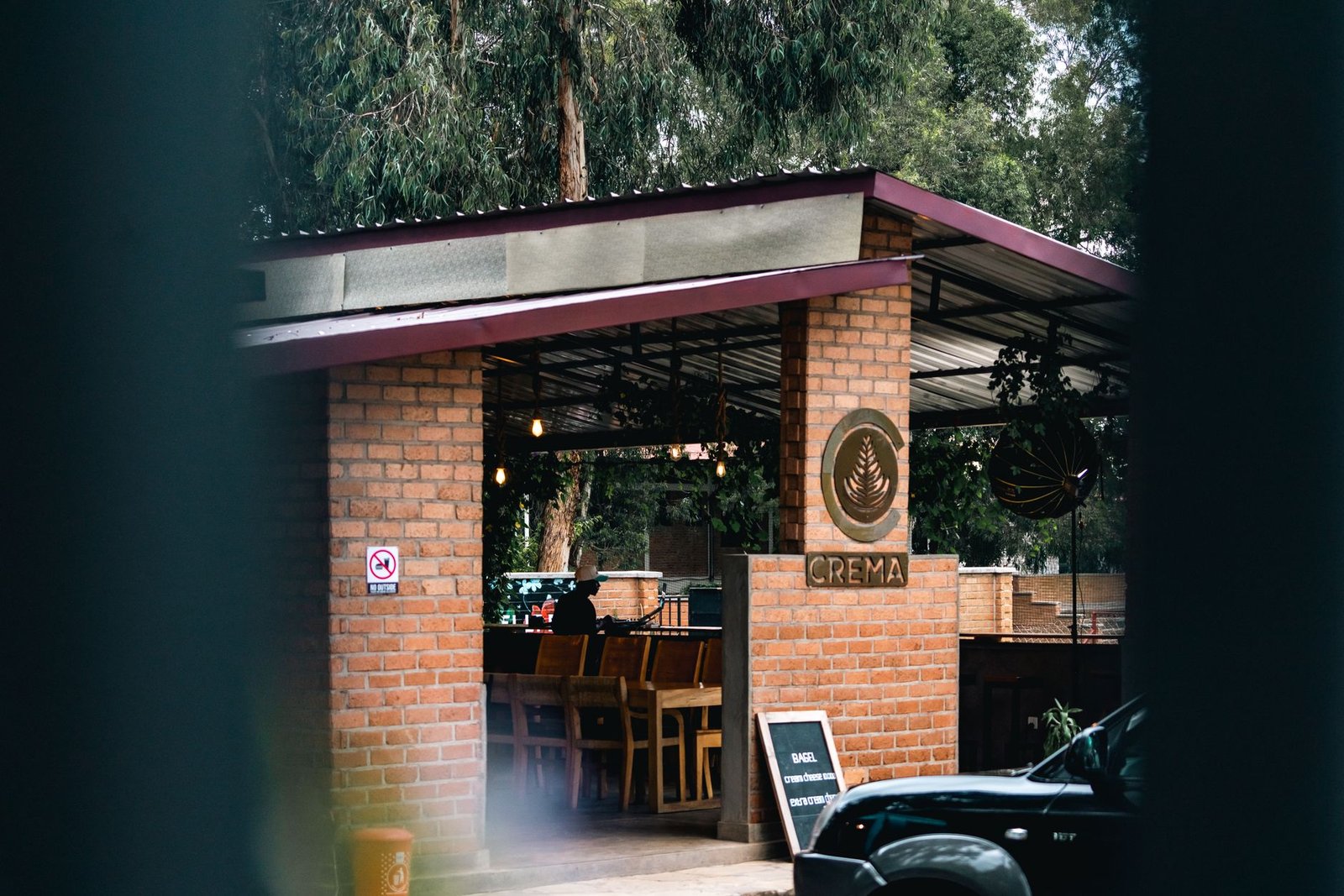 Outdoor cafe with brick walls, featuring Crema signage, seating, and greenery.