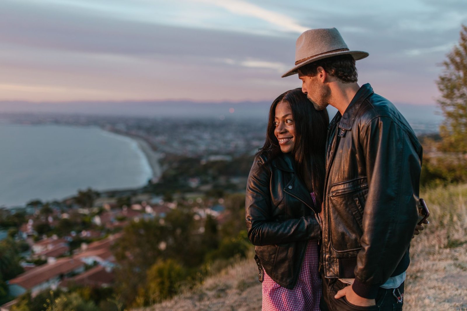 Couple embraces with a stunning coastal sunset backdrop, exuding romance and affection.