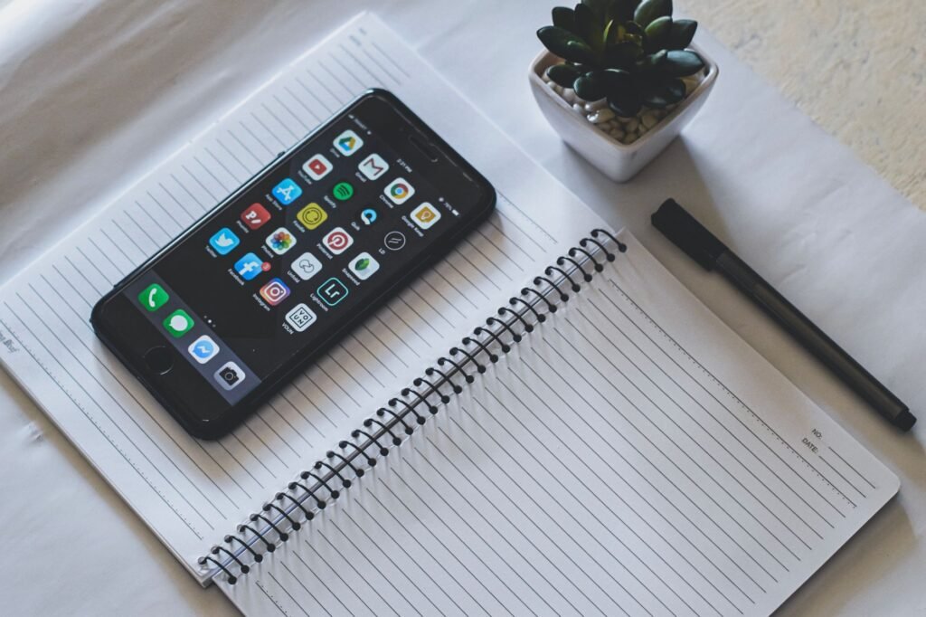 Smartphone beside a notebook and pen on a wooden table in natural daylight