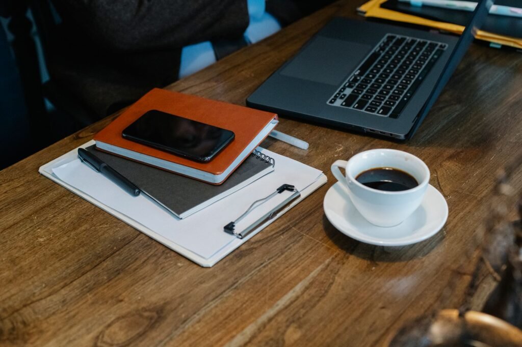 A smartphone and notebook on a plain wooden table in soft daylight