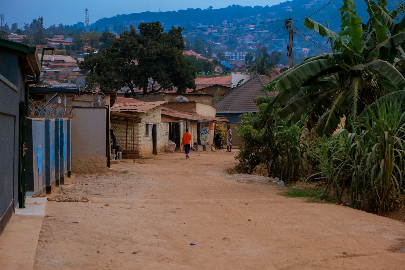 A serene evening view of an African village street with locals and lush greenery.