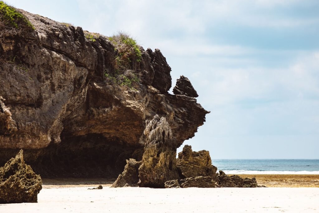 Majestic rock formations on a serene beach with clear blue skies and ocean backdrop.