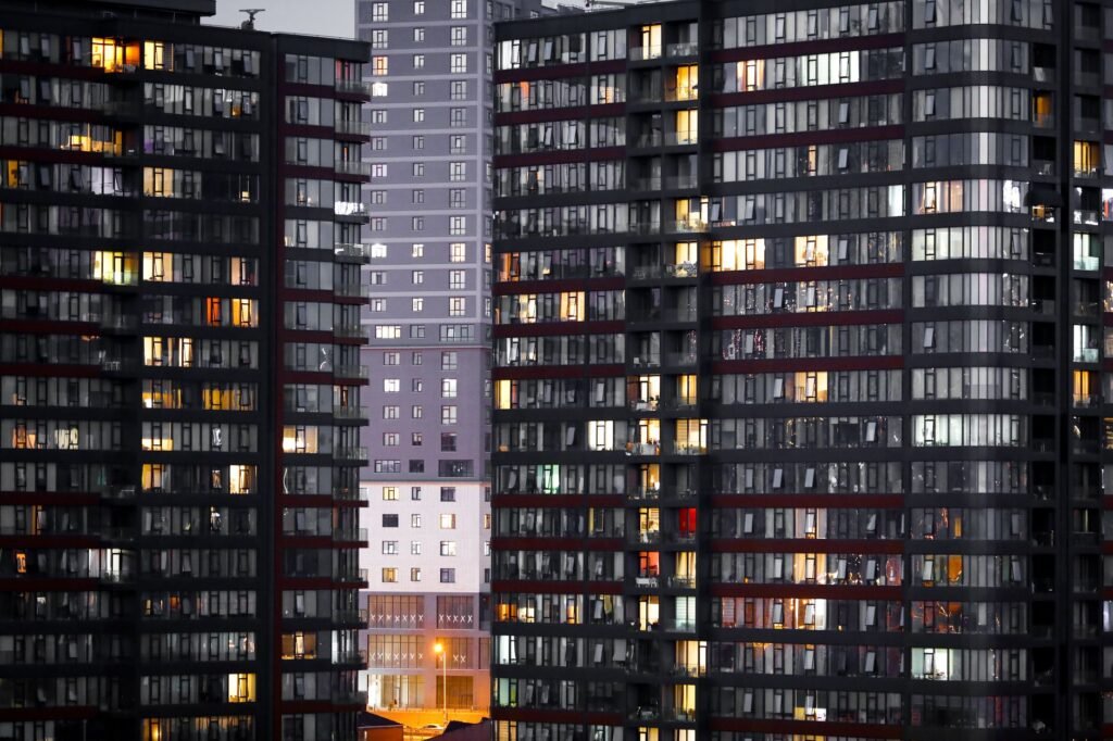 Illuminated high-rise residential buildings with glass facades at twilight in an urban setting.