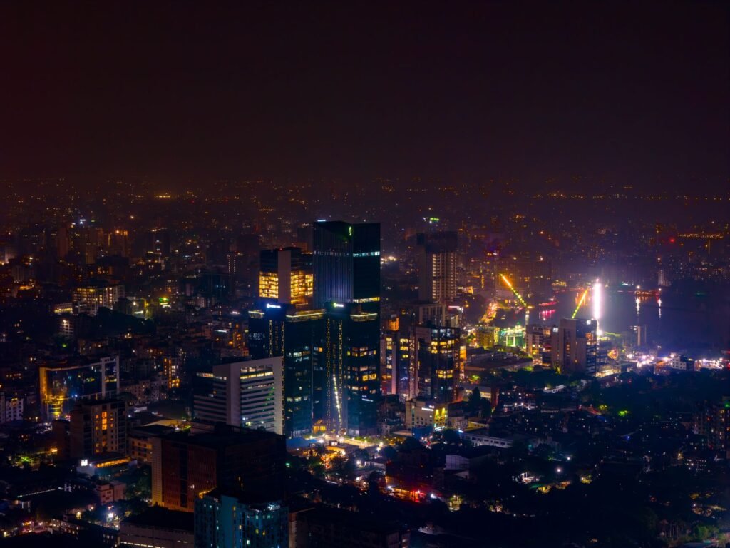 Aerial view of a bustling city skyline at night with brightly illuminated skyscrapers and streets.