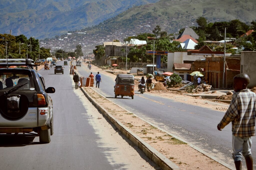 Street scene in a mountainous African town with vehicles and people, capturing daily life.