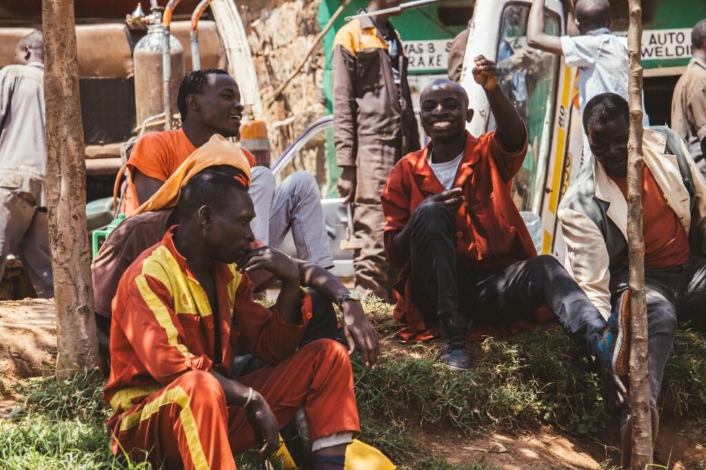 Group of mechanics in a Nairobi garage relaxing outdoors, wearing colorful uniforms.