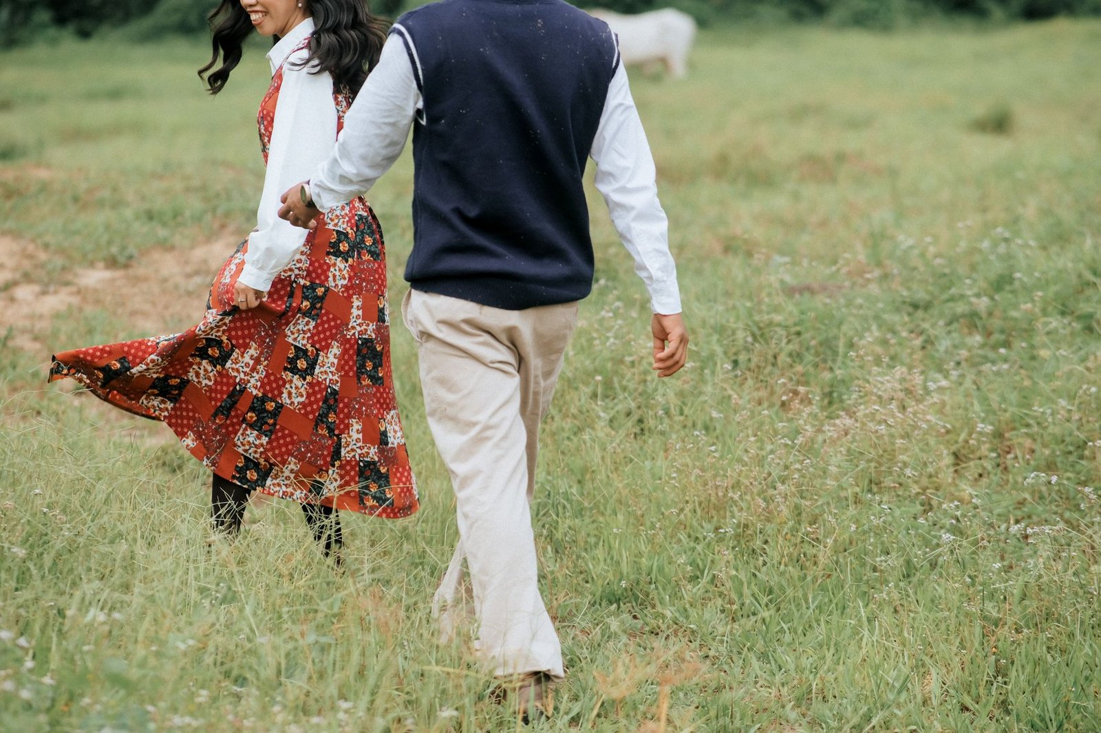 Joyful couple walking in a lush green field, holding hands and enjoying a sunny day outdoors.