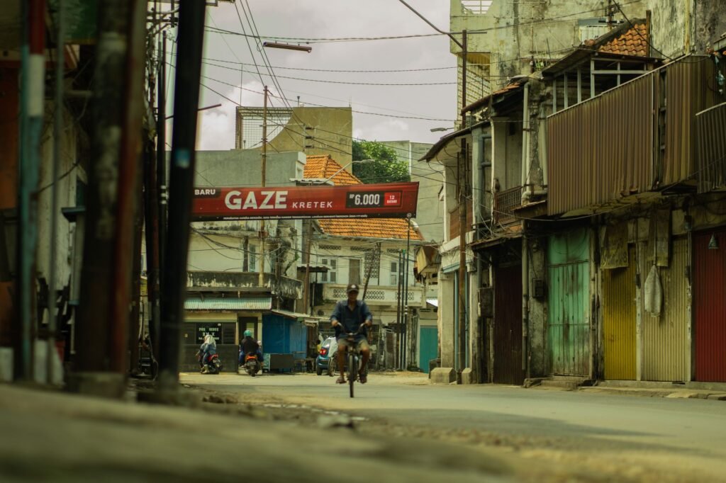 A cyclist rides through a quiet street in Jawa Timur, Indonesia, surrounded by local architecture.