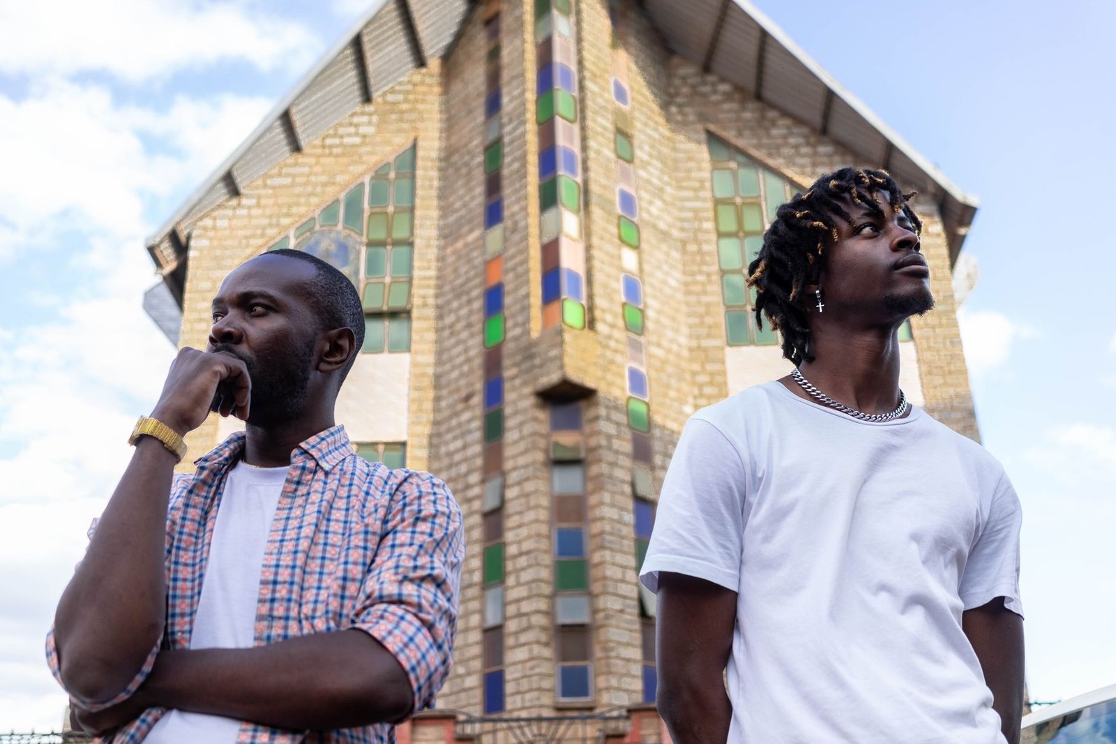 Two men standing in front of a unique building facade in Rungiri, showcasing urban fashion.