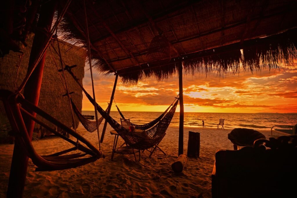 A serene sunset view at a beachside hut in Koh Kong, Cambodia, with hammocks and sandy shores.