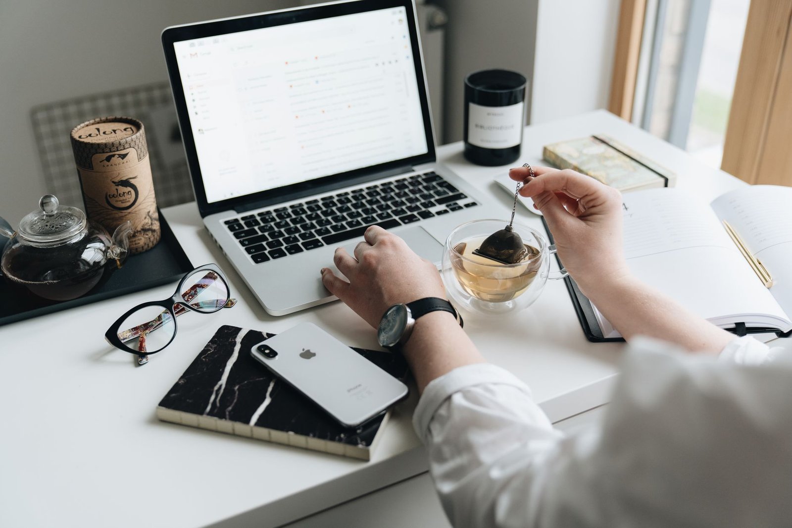 A tidy desk with an open laptop, notebook and cup of tea in daylight