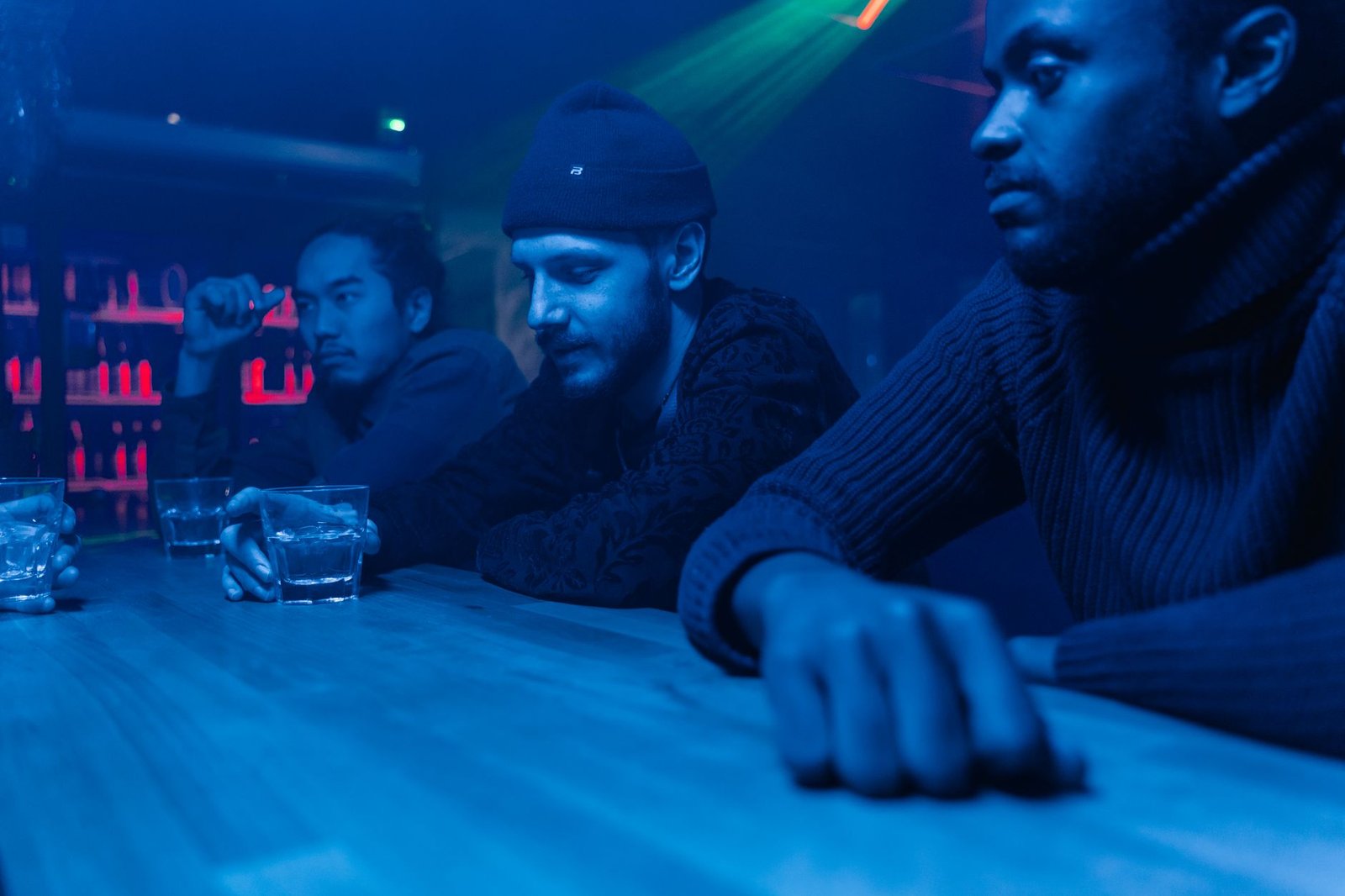 Three men enjoying a drink at a dimly lit nightclub bar, showcasing nightlife and friendship.