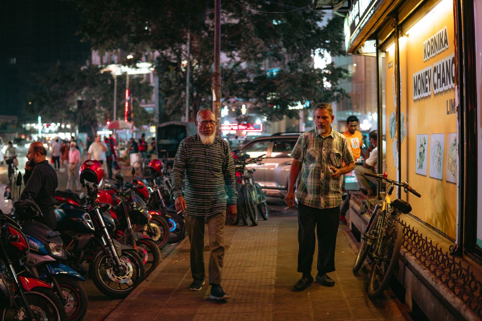 Evening urban street scene with pedestrians and parked motorbikes highlighting city nightlife.