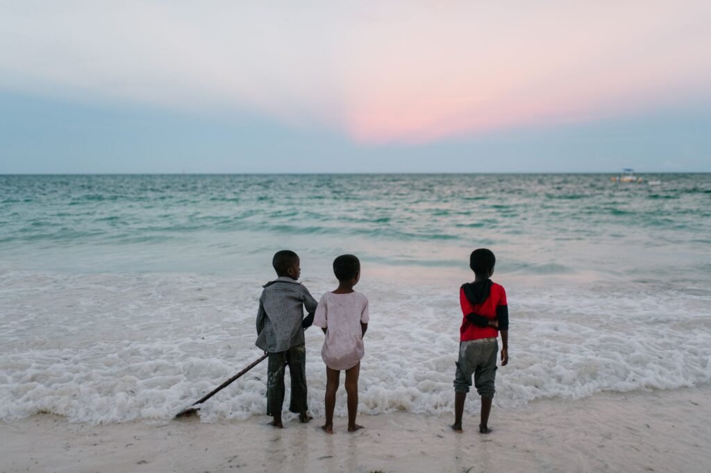Back view of company of unrecognizable ethnic boys standing on beach and enjoying view of sea at sundown in summer