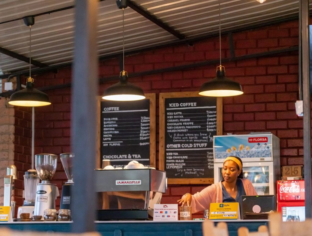 Barista at a cozy coffee shop counter, with espresso machine and menu boards in view.