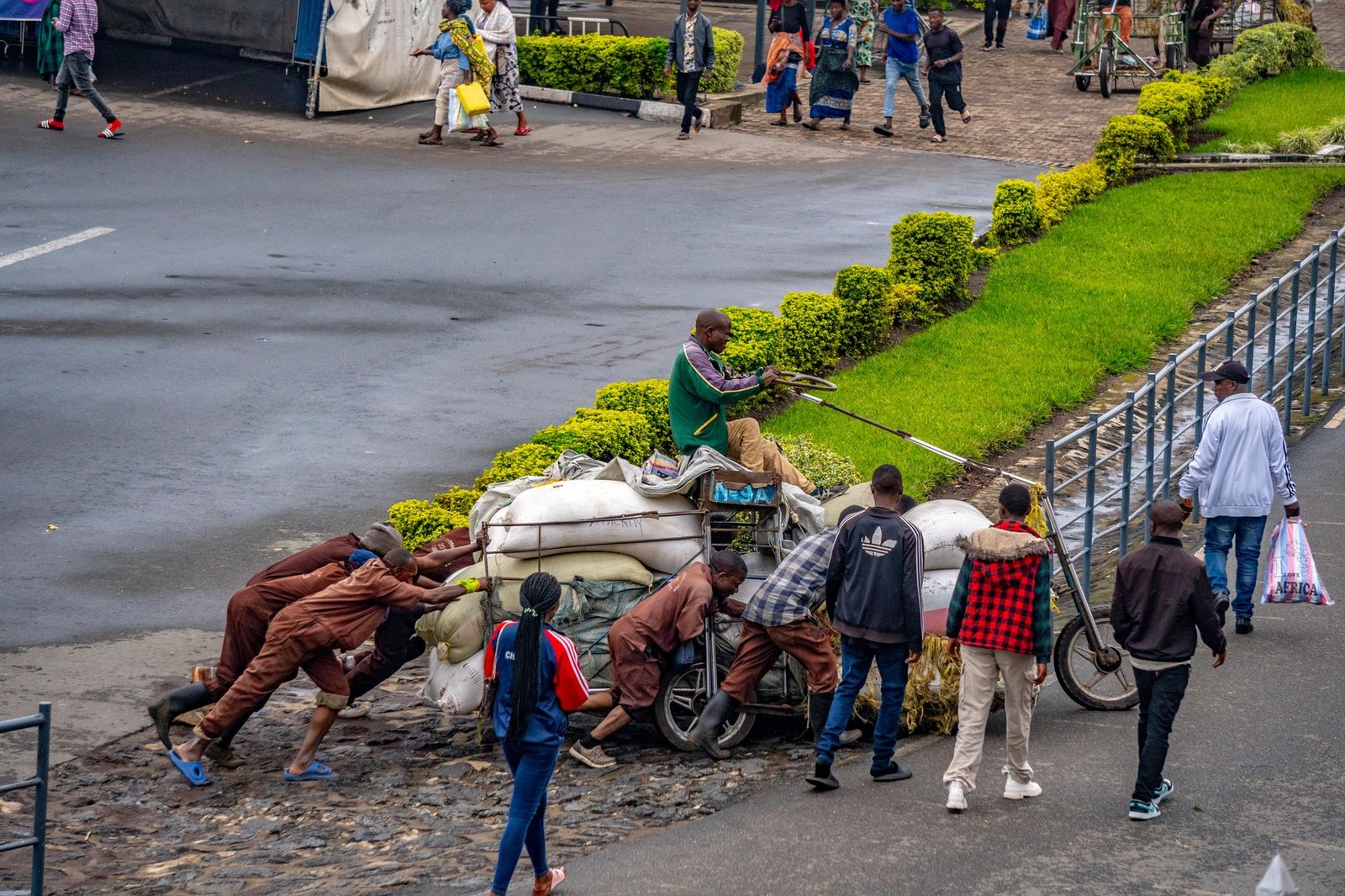 A group of people work together to push a heavily loaded cart in a bustling urban setting, showcasing teamwork.