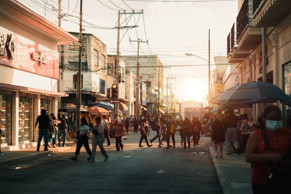 A lively city street filled with people walking and shopping during sunset, capturing urban life.