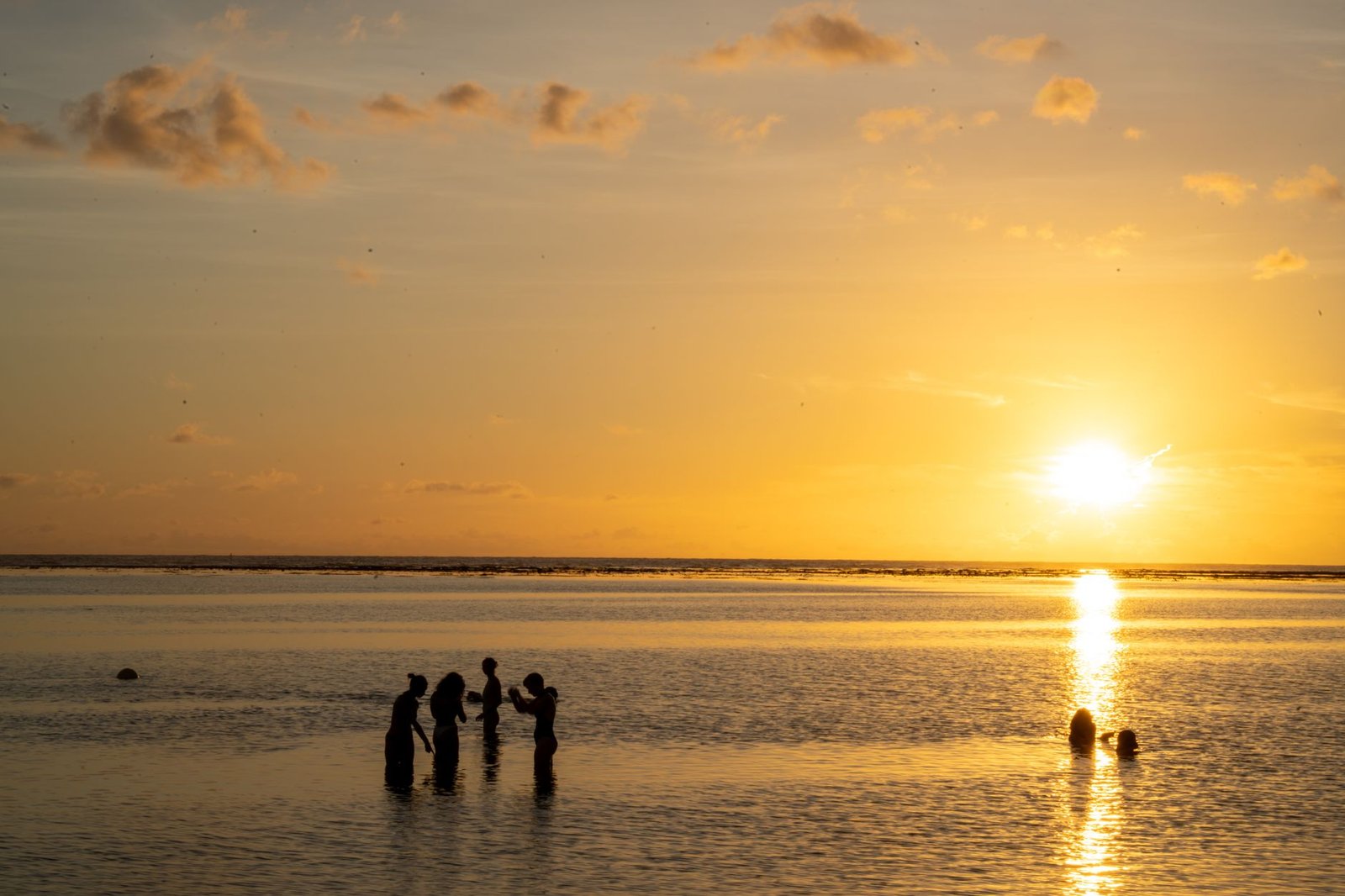 Silhouetted people enjoy the sunset at a tranquil beach in Réunion Island, creating a serene and picturesque scene.