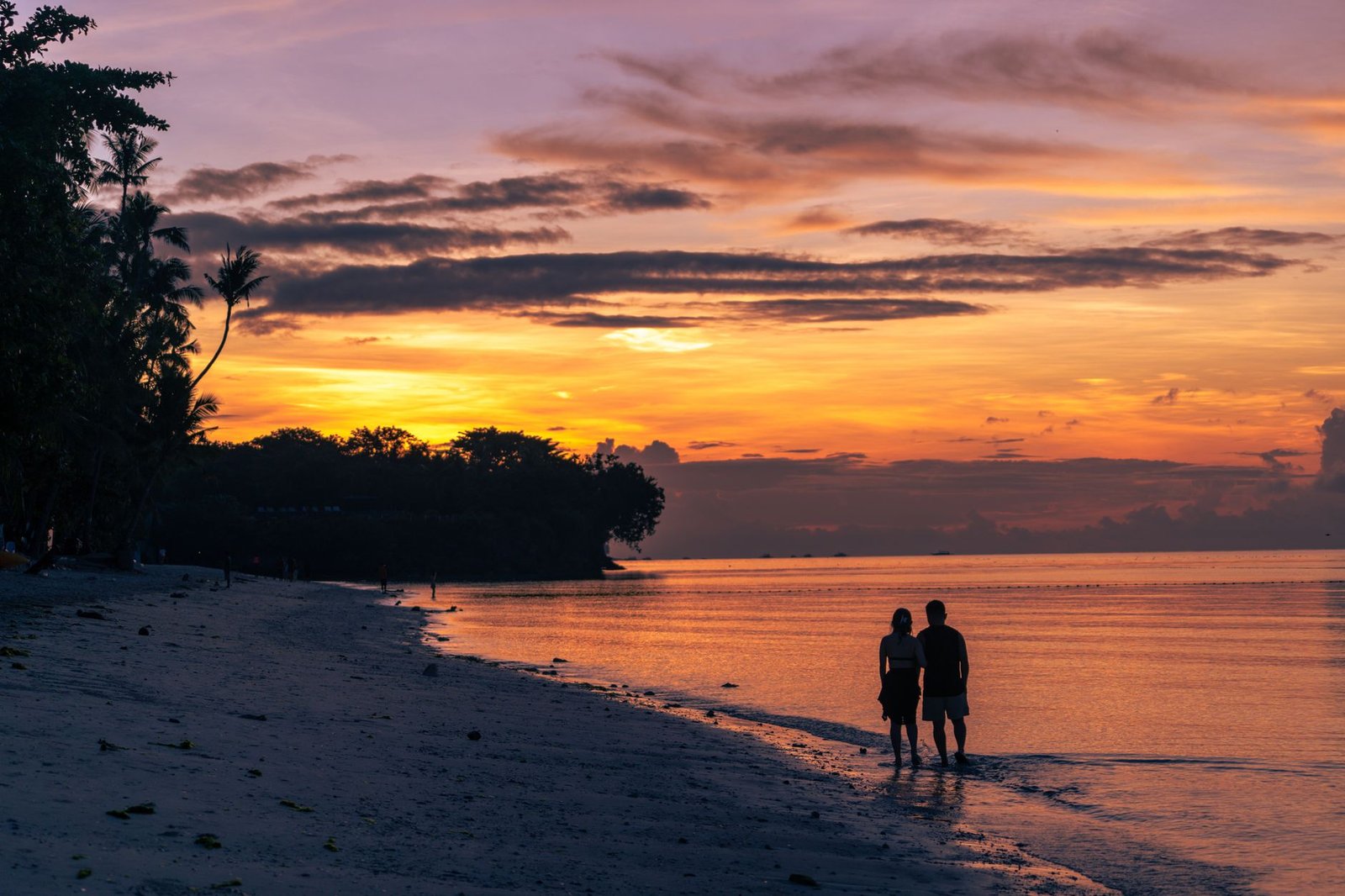 A couple walks along a serene beach at sunset, casting a romantic silhouette.