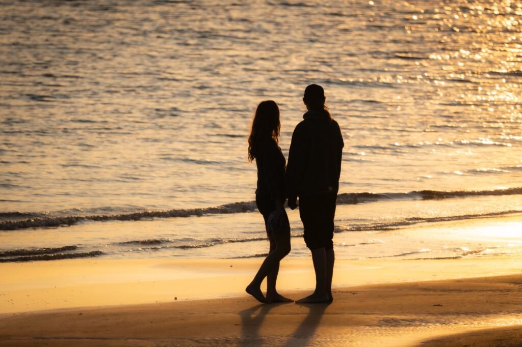 Silhouetted couple stands on a sunlit beach during a serene sunset, capturing a romantic moment.