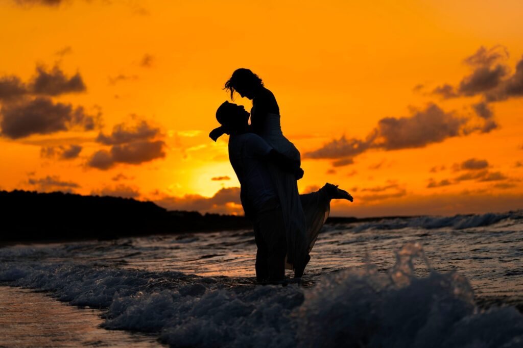 Silhouette of a couple embracing on a beach during a vibrant sunset, capturing a romantic moment.