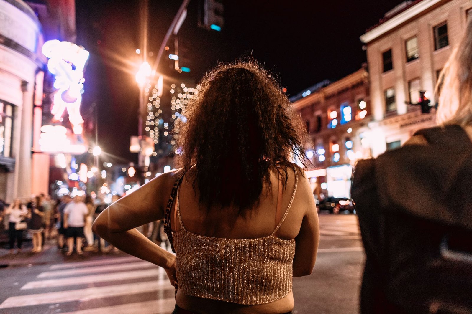 Back view of woman enjoying vibrant nightlife on a city street with neon lights.