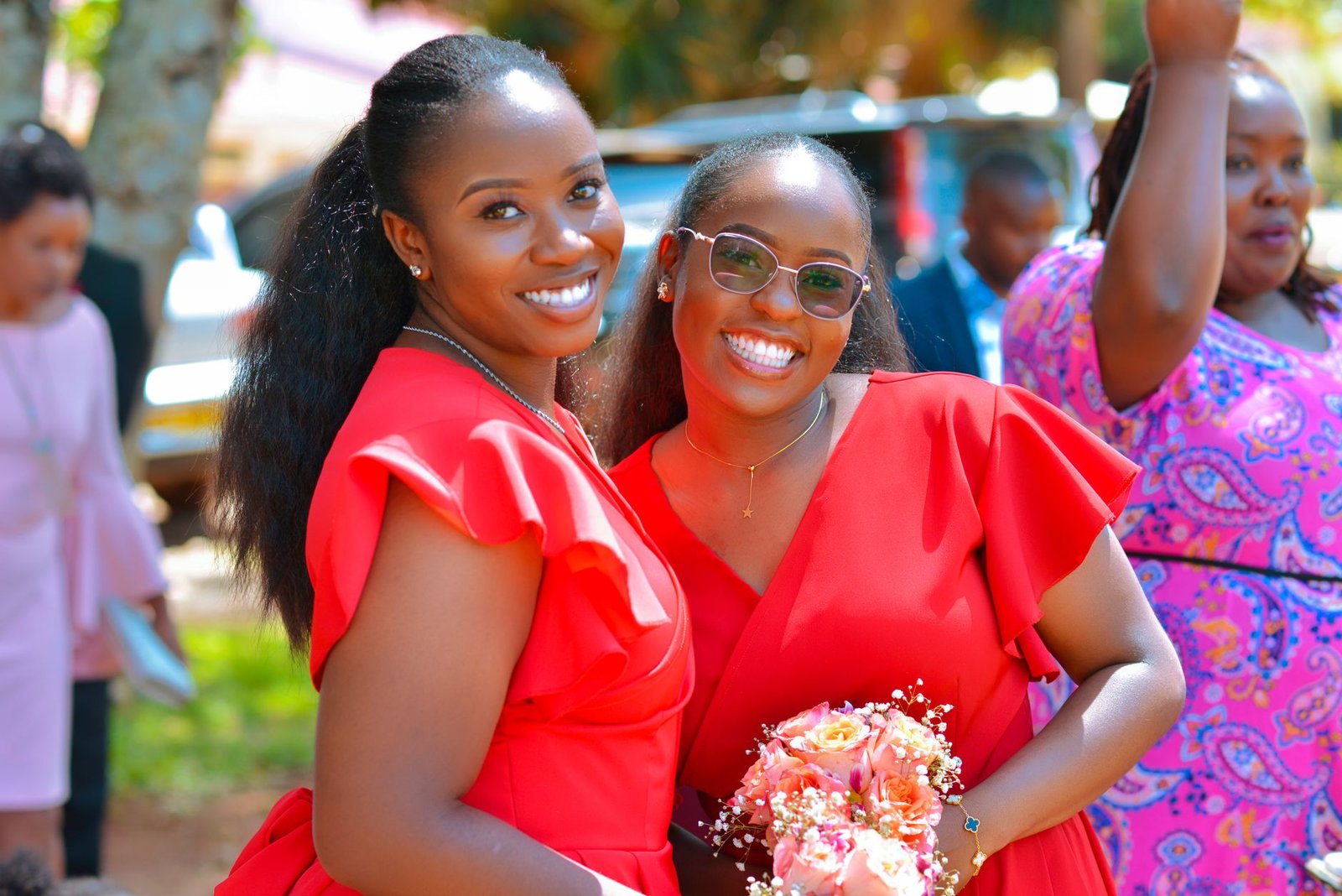 Two women in red dresses smiling at an outdoor event in Eldoret, Kenya.