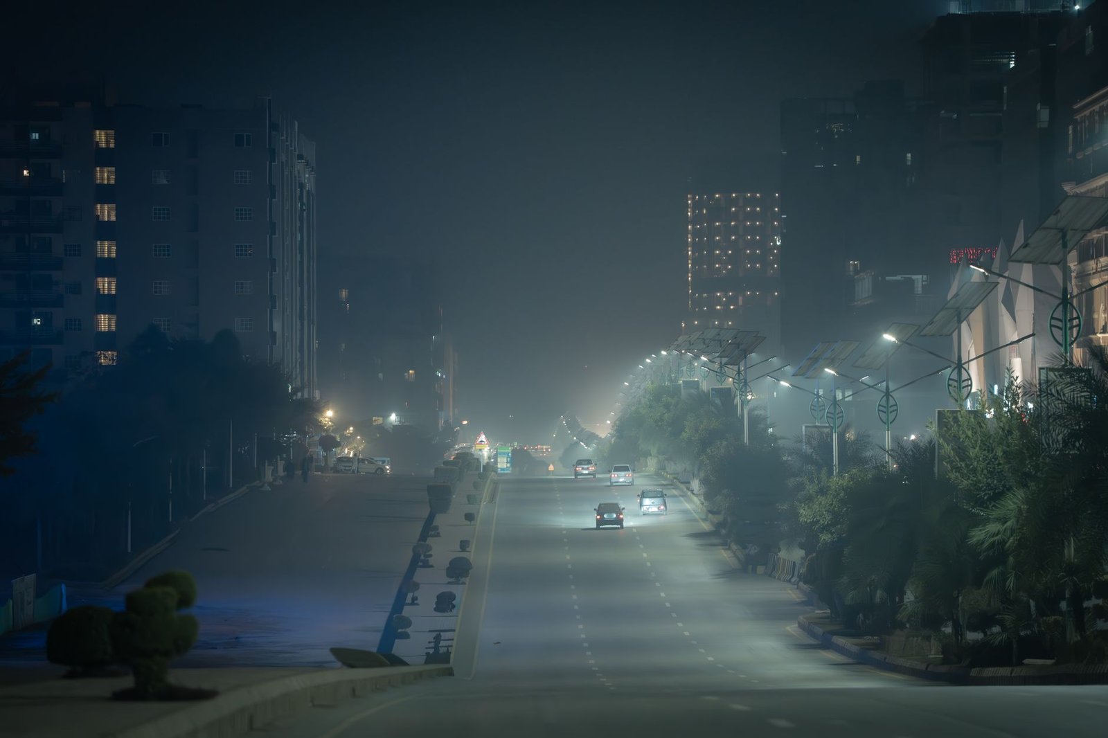 Atmospheric night street in Karachi, Pakistan enveloped in fog and city lights, creating a moody urban scene.