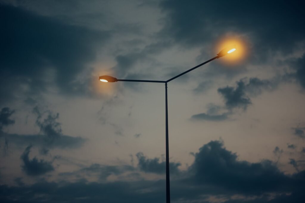 A street lamp glows against a dramatic evening sky with scattered clouds, creating a moody and atmospheric scene.